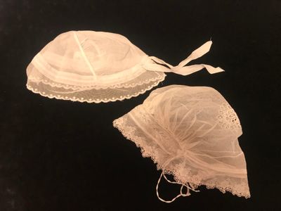 pair of white lace bras and bonnet on a black background