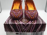des chaussures à imprimé zébré violet et orange, dans une boîte posée sur une surface blanche