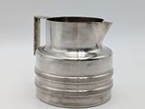 an old silver pitcher with a metal handle on a white surface