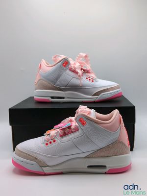 une paire de baskets blanches et roses posée sur une boîte noire