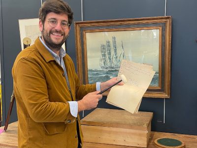 un homme souriant tenant un bout de papier devant l'image d'un bateau