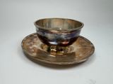 une tasse et une soucoupe en argent posées sur une soucoupe, sur une table blanche