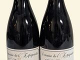 two bottles of red wine sitting next to each other on a white surface