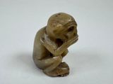 figurine of a monkey sitting on a white surface with his hands on his face