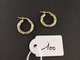 a pair of gold hoop earrings and a tag on a black surface