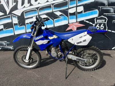 une moto tout-terrain bleue et blanche garée devant un mur recouvert de graffitis