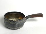 une petite casserole avec un manche en bois posée sur une surface blanche
