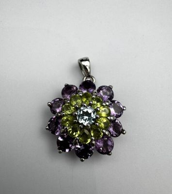 un gros plan d'un pendentif en forme de fleur verte et violette posé sur une surface blanche