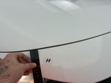 a person holding a ruler in front of a white car