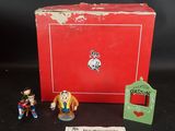 La boîte est rouge et contient deux petites figurines.