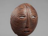 a wooden mask on a stand with a gray background