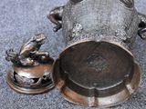 a silver vase with a frog on it next to a small figurine