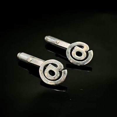 paire de boutons de manchette en argent sur un support noir avec un fond noir
