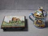 a small box with a painting on it next to a coffee pot