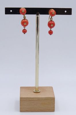 boucles d'oreilles ornées de perles rouges, présentées sur un support, sur fond blanc