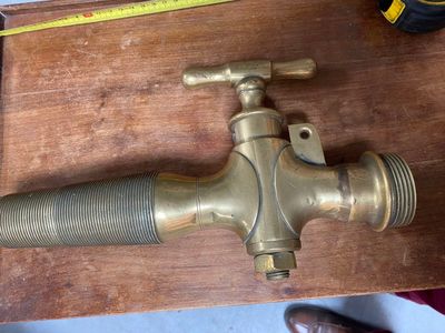 a brass faucet on a wooden table with a measuring tape