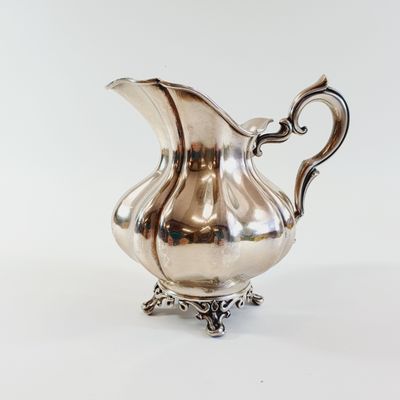an image of a silver pitcher on a stand on a white surface