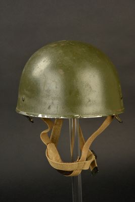un vieux casque vert posé sur un socle transparent, sur fond noir