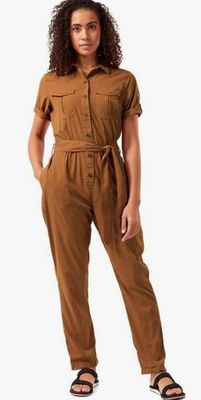 a woman wearing a brown jumpsuit and sandals stands in front of a white background