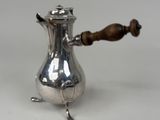 une cafetière ancienne en argent avec une poignée en bois, posée sur une surface blanche