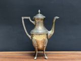 an antique silver tea pot on a wooden table against a black wall