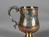 une vieille coupe en argent munie d'une anse, posée sur une surface grise