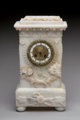 une petite horloge blanche avec un cadran doré, posée sur un socle