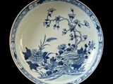 blue and white plate with flowers and birds on it on a black background