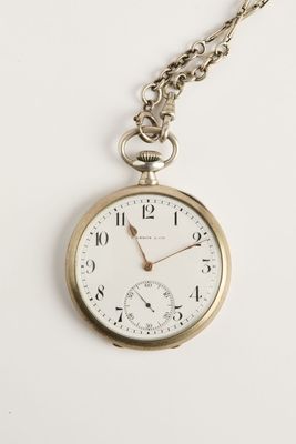 une vieille montre de poche avec une chaîne, posée sur une surface blanche