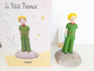 figurine représentant un garçon en costume vert, debout à côté d'un livre