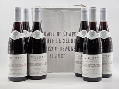 three bottles of red wine sit in front of a silver box
