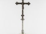 a silver cross on a pedestal with a white background