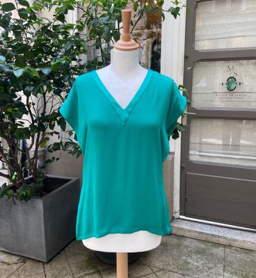 un haut vert posé sur un mannequin devant une plante en pot
