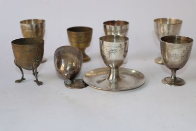 cinq gobelets en argent et une coupe en argent posés sur une table blanche