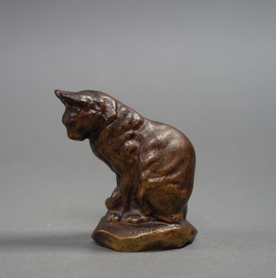 bronze statue of a cat sitting on a rock on a gray surface