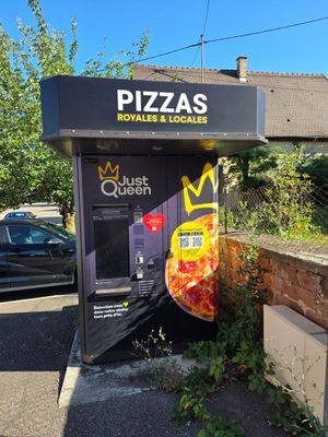 un distributeur automatique sur lequel est posée une pizza, au milieu de la rue