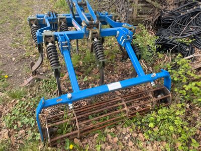 une charrue bleue posée dans l'herbe à côté d'un tas de fils