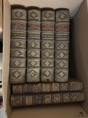 Plusieurs vieux livres sont empilés dans une boîte en carton posée sur une table