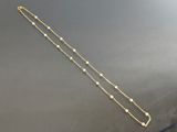 a long gold chain with white beads on a black surface