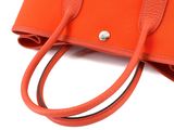 an orange handbag with two handles and a strap on a white background