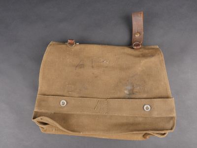 un vieux sac en toile marron muni d'une poignée en cuir, posé sur une surface grise