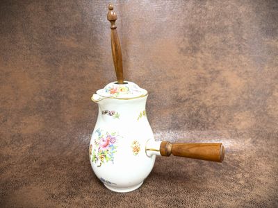 a small white vase with a wooden handle on a brown surface