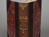 an old book with a red cover sitting on top of a table