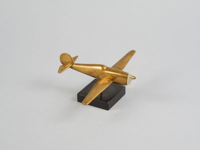 figurine d'avion dorée sur socle noir, sur fond blanc