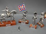 four silver figurines of soldiers on wooden bases with a flag