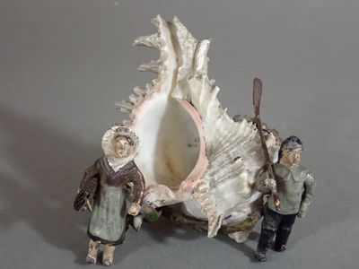 two figurines of people standing in front of a seashell