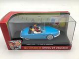une petite voiture dans une boîte posée sur une surface blanche, avec une boîte rouge à côté