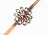 une broche en forme de fleur, argentée et rouge, ornée de perles et fixée sur une tige en bois