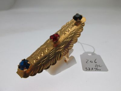 une image représentant une broche en forme de plume en or, ornée de pierres rouges et bleues