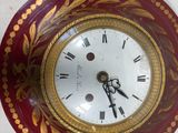 a red and gold clock sitting on a white surface
